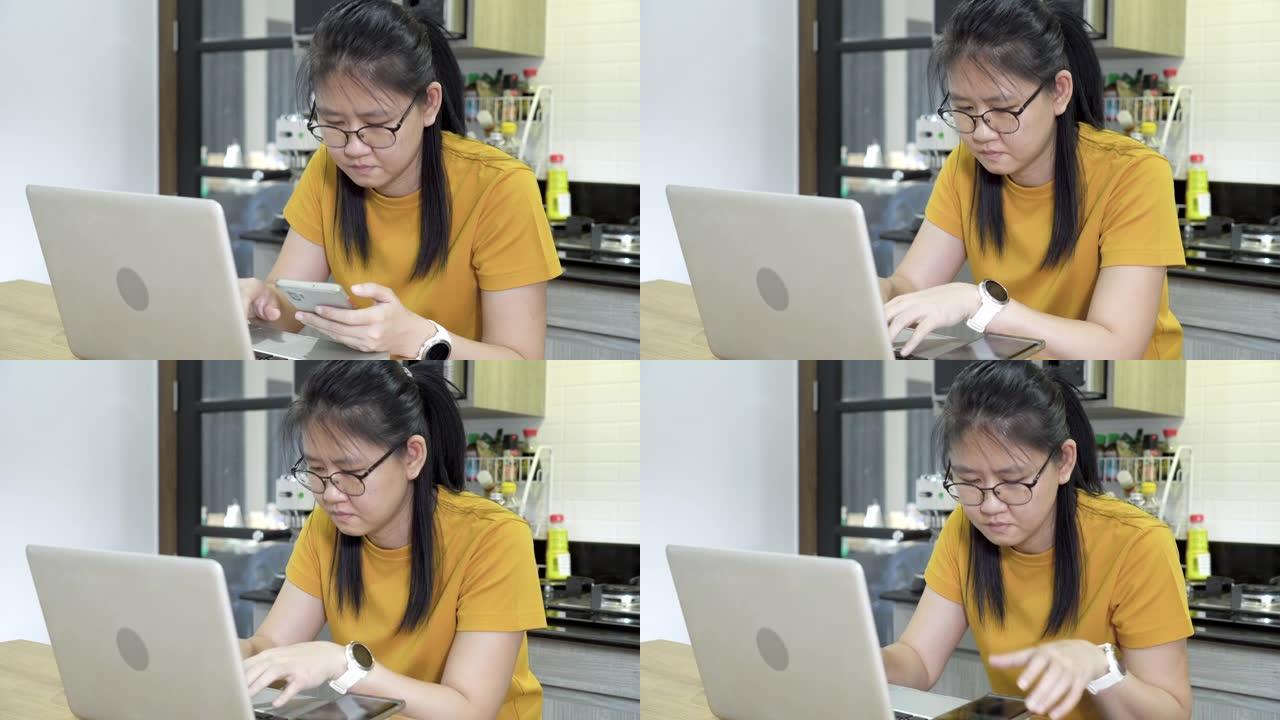 亚洲女性自由职业者使用笔记本电脑在家里的厨房里工作。