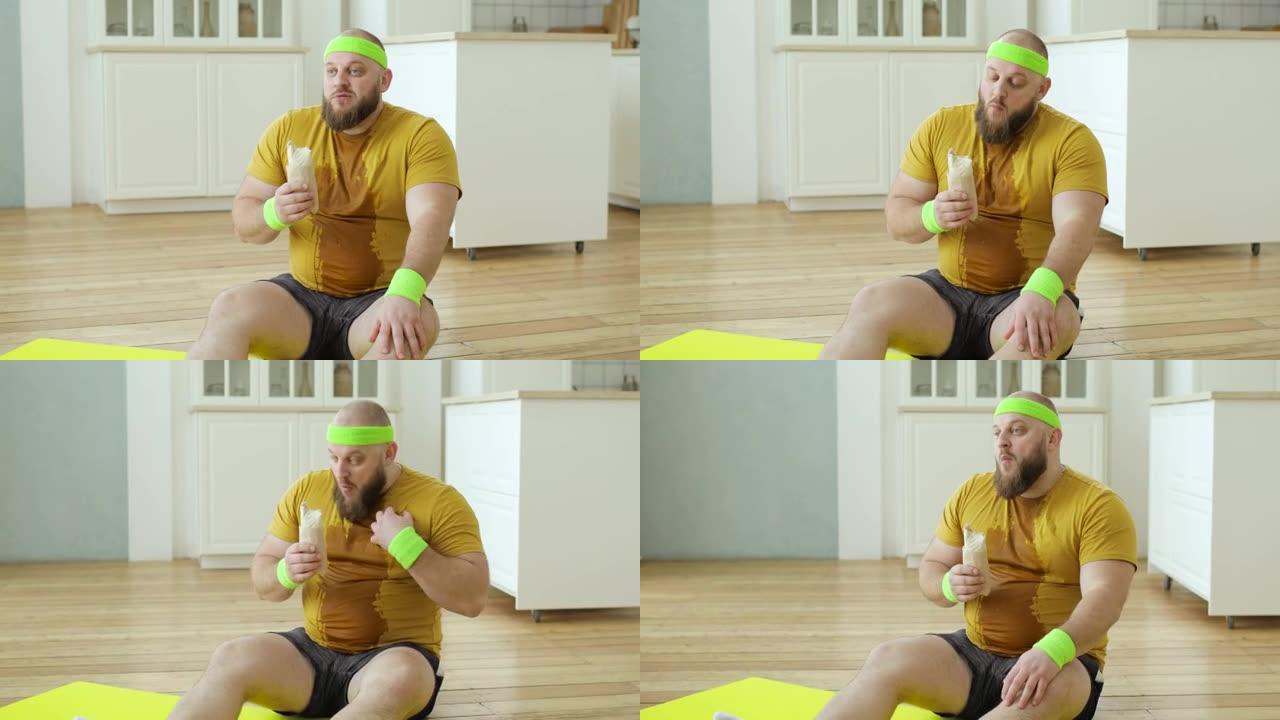 穿着黄色运动服的汗流浃背的胖子在家坐在健身垫上吃丹纳尔