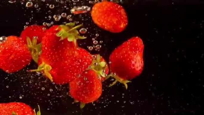 漂浮在水中的草莓的详细拍摄。彩色浆果以慢动作沉入液体中。