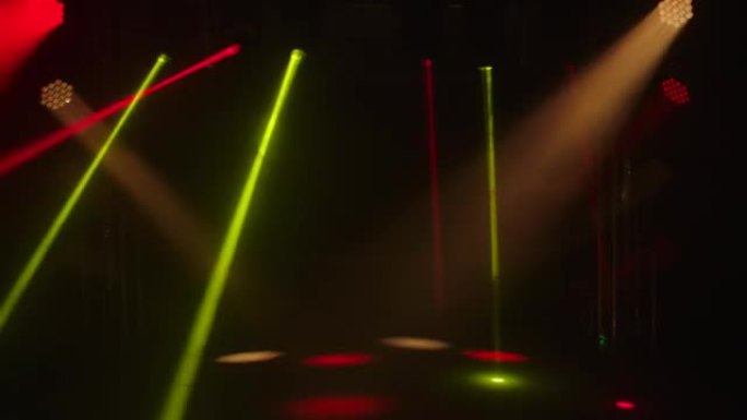 舞台上的彩色激光。聚光灯在黑暗的烟熏工作室中旋转，旋转并发出红色和黄色光束。全息图显示。假日和聚会的