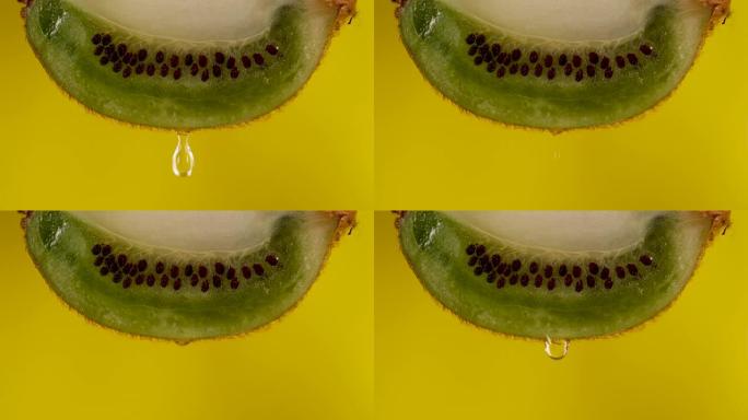 宏观滴水滴落的新鲜绿色猕猴桃切片和黄色背景上的种子果实。慢动作水滴从多汁的新鲜成熟美味切片猕猴桃，特