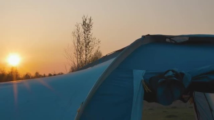 傍晚。一个大蓝色帐篷的特写。通过帐篷的窗户可以看到地面。地平线上的红色日落。太阳的光线在帐篷上滑行