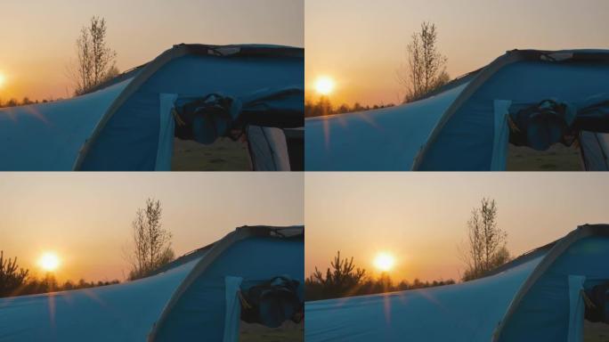 傍晚。一个大蓝色帐篷的特写。通过帐篷的窗户可以看到地面。地平线上的红色日落。太阳的光线在帐篷上滑行