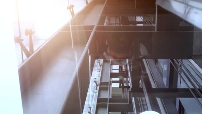 现代商业建筑中的移动电梯。电梯上升。向上看。太阳在左上角闪烁。电梯内部的机械结构。镜子反映了乘客的身
