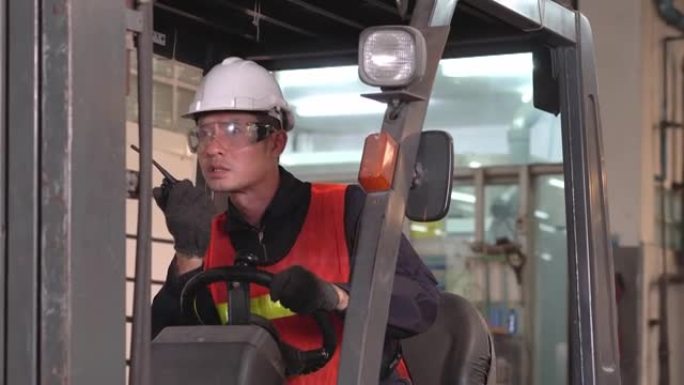 亚洲男性仓库工人在重工业制造工厂与驾驶叉车的同事通过无线电电话或对讲机交谈。努力工作的人的肖像。运输