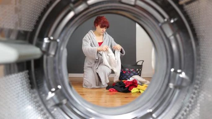 女人在洗衣服前整理脏衣服。家庭主妇坐在篮子里整理衣服。从洗衣机内部观察。