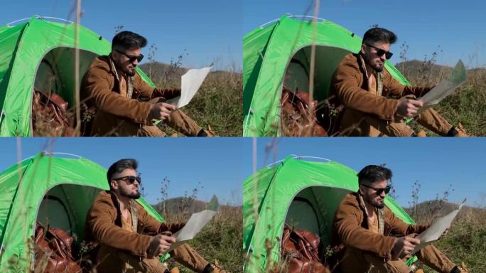 大胡子迷人的年轻徒步旅行者带着背包在山地露营帐篷看地图