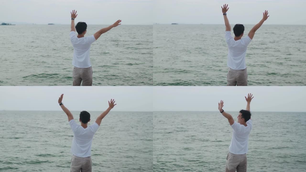 快乐的亚洲男性庆祝活动在假日周末举起双臂成功。英俊的白人旅行者站在海滩上，看着海景。