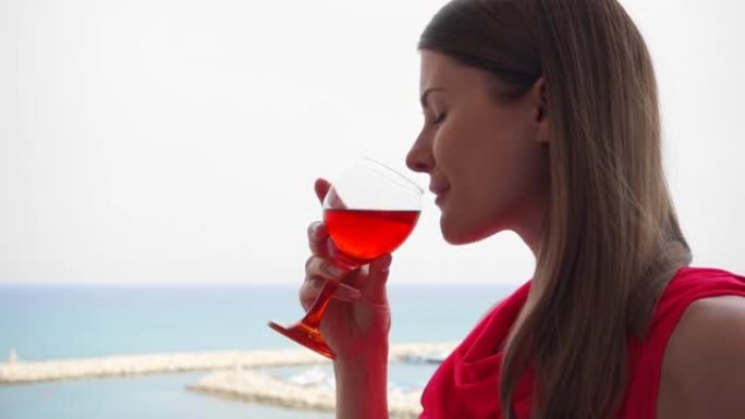 女人从露台上欣赏海景。度假女性在阳台上慢动作喝玫瑰酒