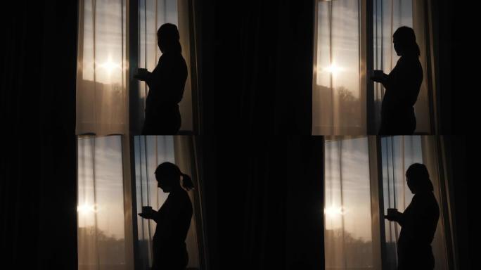 窗前一个女人的剪影，喝着热饮，看着冉冉升起的太阳