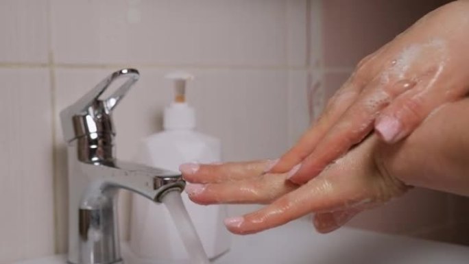 一个女人在浴室用肥皂和水洗手的特写镜头。