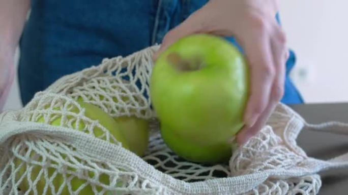 水果白网。网里有很大的青苹果。用左手打开网，一个接一个地给苹果。健康饮食。水果有用性概念