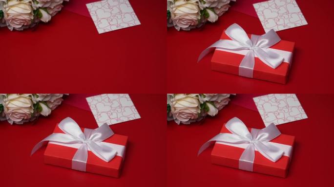 带有白色丝带蝴蝶结的礼品盒落在红色桌子上。节日背景，带有情人节、一束玫瑰、一个信封、情人节和装饰性的