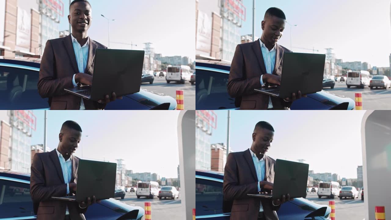 一名非裔美国自由职业者手中拿着一台笔记本电脑，靠在正在充电的豪华电动汽车上。一边给汽车充电一边工作。
