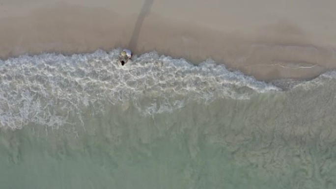 一对年轻夫妇站在海洋海岸的岸边。海浪冲刷了他们的脚。从上方观看