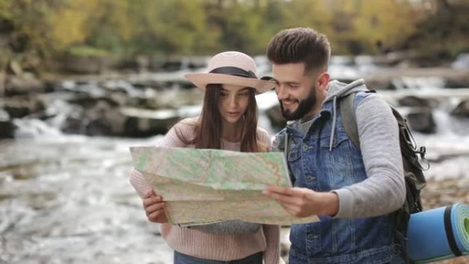 一名年轻女子和一名男子正在讨论徒步旅行的路线。他们手里拿着地图。背景中的山河。4K。