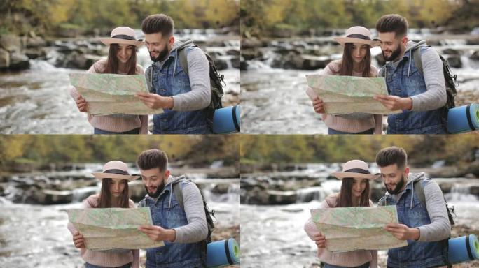 一名年轻女子和一名男子正在讨论徒步旅行的路线。他们手里拿着地图。背景中的山河。4K。