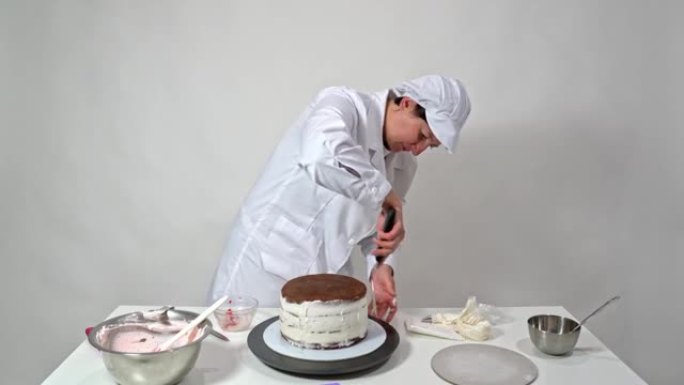 面包师的正面照片使用抹刀仔细修饰奶油蛋糕的侧面。