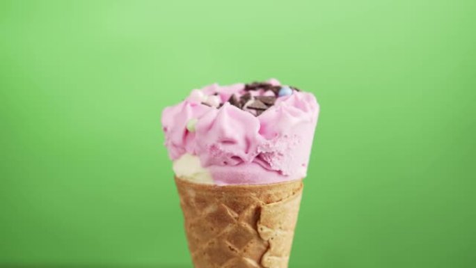 浆果冰淇淋蛋卷，绿底有巧克力片，旋转。美味的自制白色和粉红色冰淇淋，配五颜六色的糖洒。
