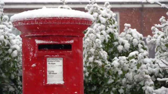 在飘落的雪中关闭传统的红色邮筒