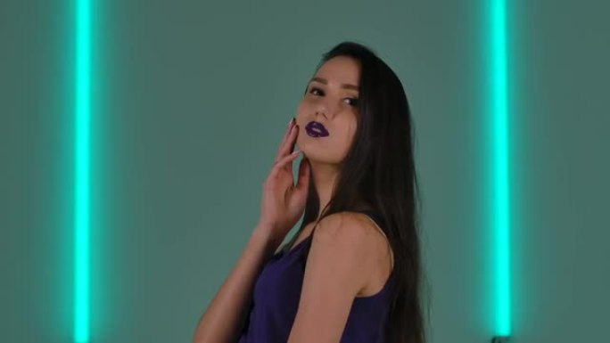 年轻时尚女子的肖像在镜头前撒娇。长发和紫色唇膏的时装模特在明亮的霓虹灯背景下摆姿势。特写。慢动作