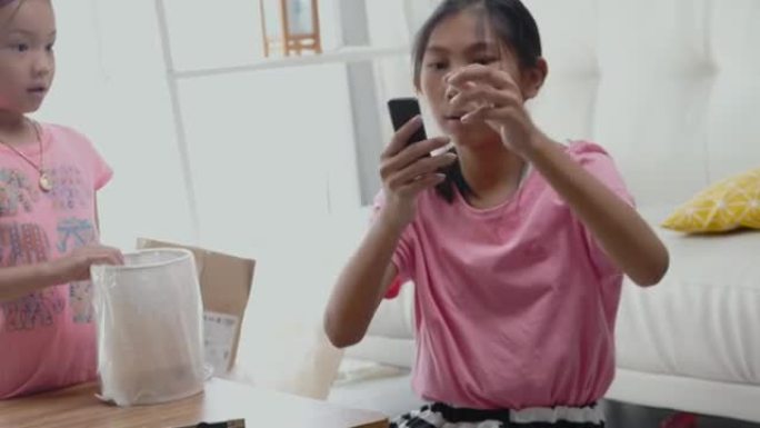 快乐的亚洲儿童收到网上购物的商品，并在家里打开窗户附近的新电灯，生活方式概念。