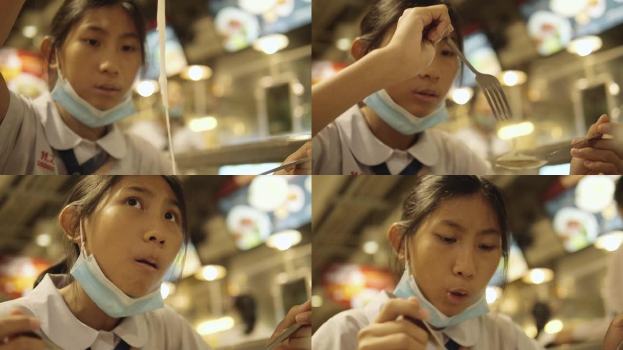 穿着制服的亚洲女学生在美食广场吃热面条汤，一边休息，生活方式理念。