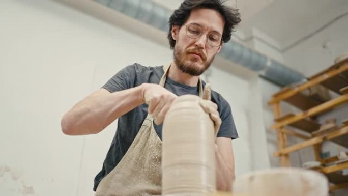 专业男艺术家创作陶瓷花瓶，用陶轮上的粘土工作，视图下方，慢动作