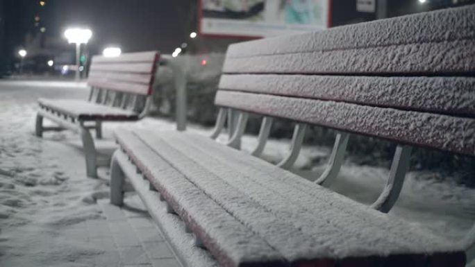 在城市公园里，雪地里的长凳。夜。