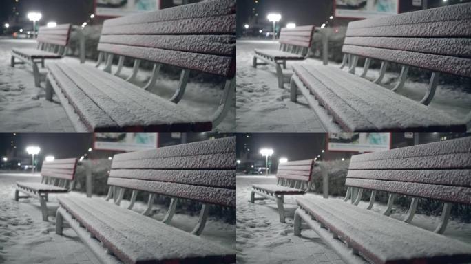在城市公园里，雪地里的长凳。夜。