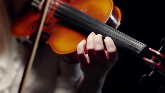 拉金发女人的小提琴。小提琴指板上的手指，黑色背景工作室拍摄的特写镜头