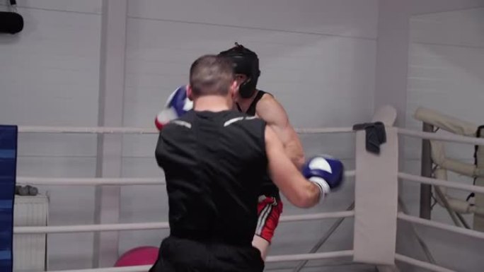 教练训练拳击手男子头盔，手套和腹股沟保护在战斗环。两名拳击手在拳击训练中战斗。搏击俱乐部的男性有氧训