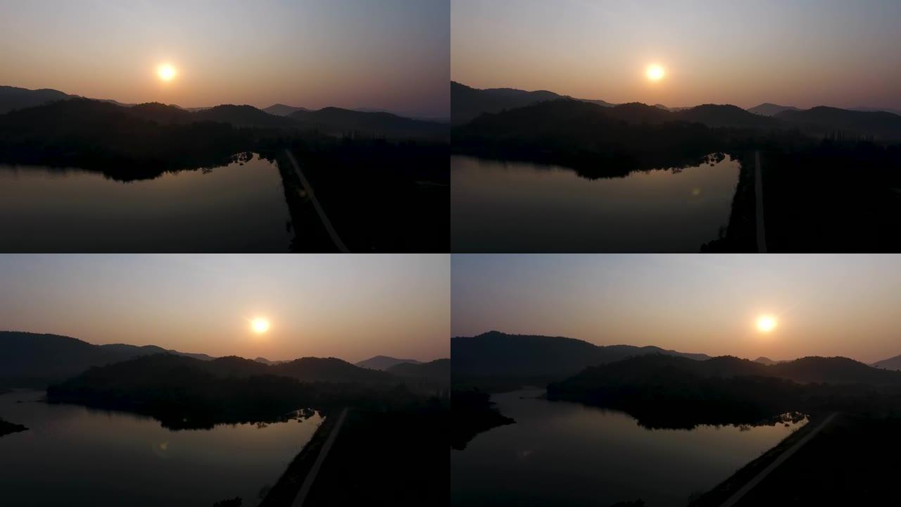 美丽的湖泊的鸟瞰图被清晨反射在水面上的山丘所环绕，天空中温暖的阳光在红色和蓝色中产生了温暖的亮光，令