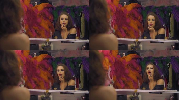 女演员漂亮女孩在更衣室的镜子前用红色唇膏画嘴唇，化妆