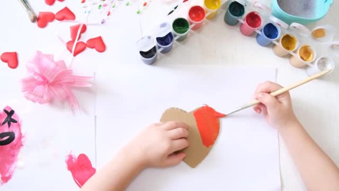 制作自制贺卡的孩子。一个小女孩画一颗心作为母亲节或情人节的礼物。