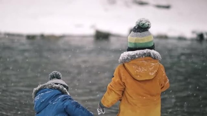 小双胞胎男孩在冬天在河边玩雪。可爱的幼儿玩得开心，把雪球扔进水里。