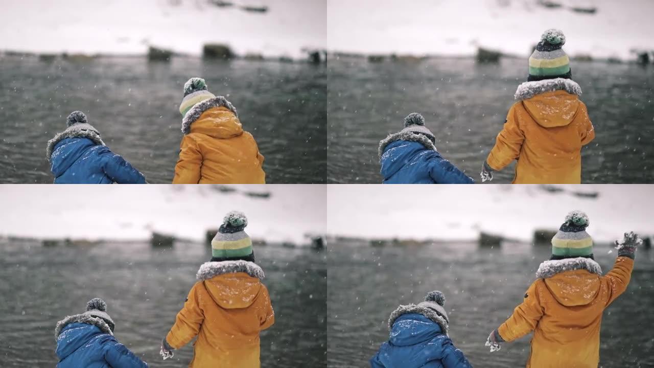 小双胞胎男孩在冬天在河边玩雪。可爱的幼儿玩得开心，把雪球扔进水里。