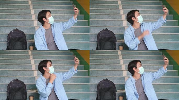 由于新的新型冠状病毒肺炎规定，大学生男子戴着防护罩，使用手机进行视频通话，并在校园内保持安全距离。