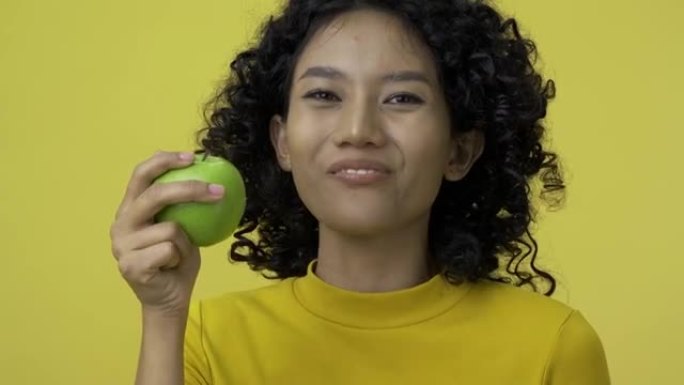 年轻女子在黄色背景下吃青苹果的肖像。