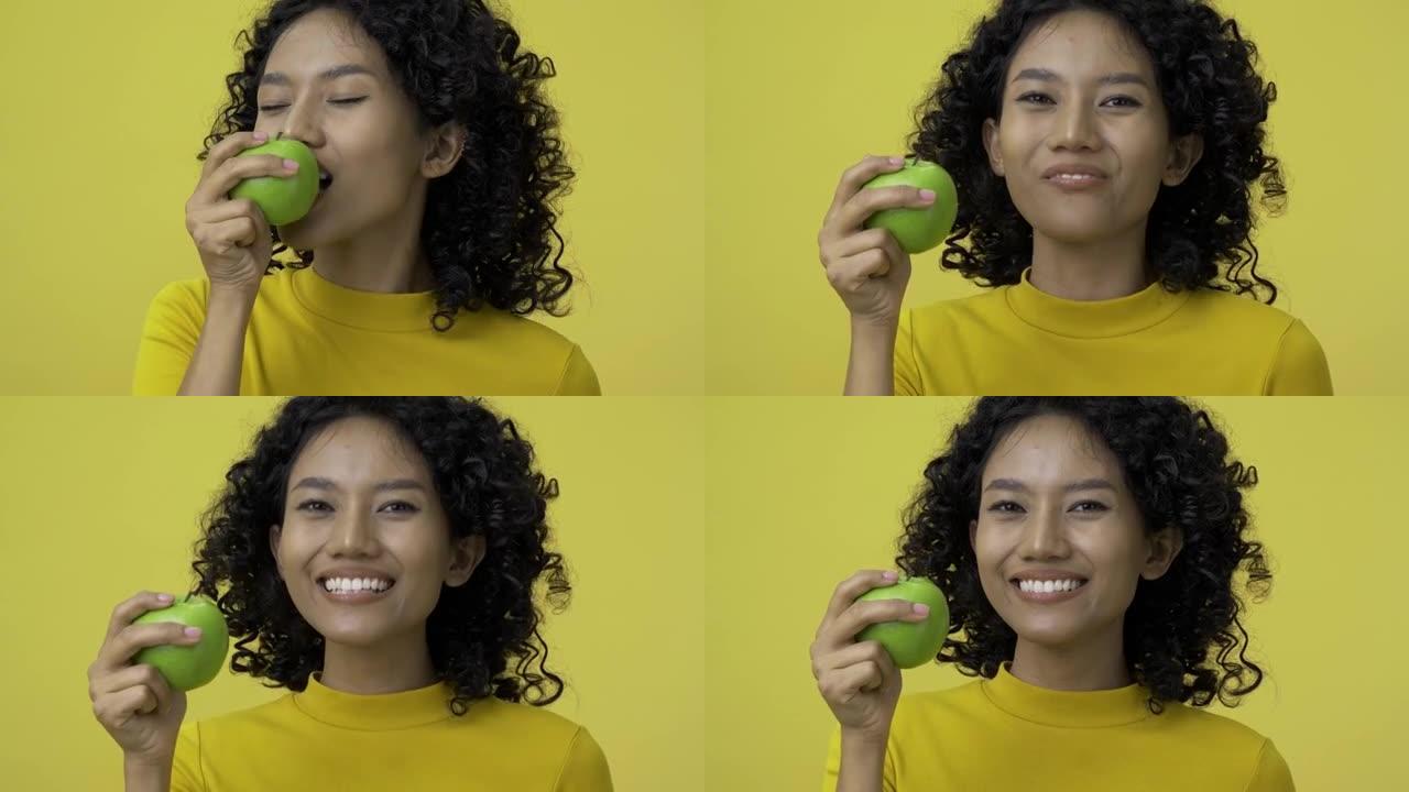 年轻女子在黄色背景下吃青苹果的肖像。