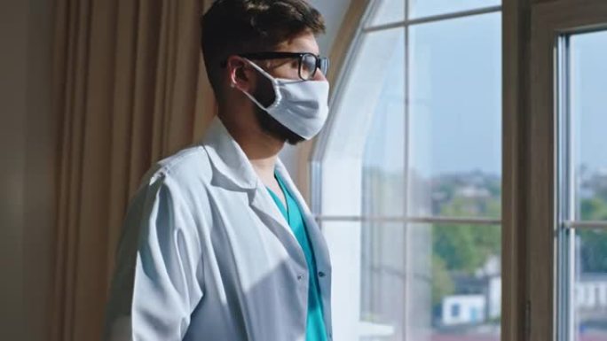 在一家现代医院里，戴着防护口罩的年轻医生稍事休息，他透过全景窗户看了一眼，并有一张思考的脸。在阿里·