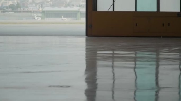 关闭带有大玻璃窗的巨大飞机机库门，在slowmo机场着陆场附近的环氧地板上铸造出闪亮的反射