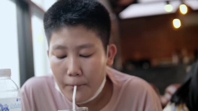 亚洲男孩在餐厅等食物时用稻草喝水，生活方式概念。