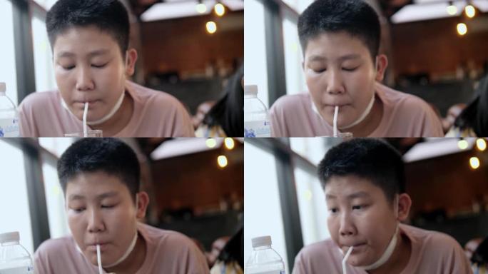 亚洲男孩在餐厅等食物时用稻草喝水，生活方式概念。
