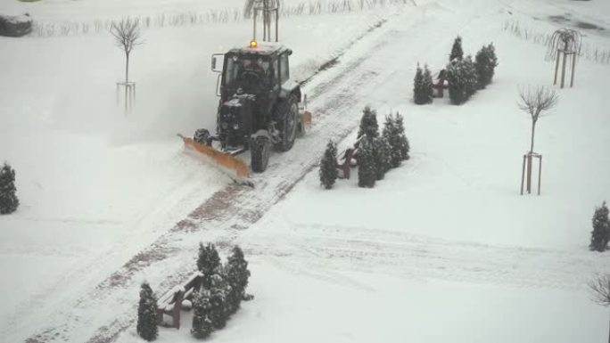 拖拉机-挖掘机清除城市院子里的积雪。公用事业的工作