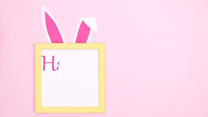 复活节快乐写在框架内，兔子耳朵和爪子在柔和的粉红色背景上。停止运动
