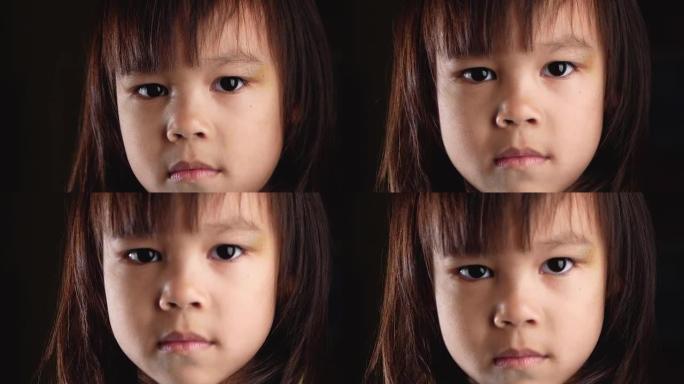 可爱的小女孩的特写脸肖像在家里的黑暗房间里，悲伤和怨恨地看着相机。不幸的童年的概念。