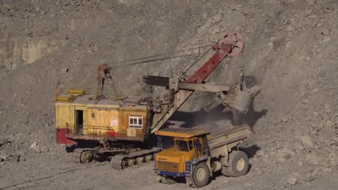 一辆巨大的采矿挖掘机将土壤倒入一辆大型多吨黄色采矿卡车的车身中