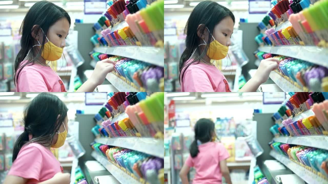 戴着口罩的亚洲女孩在家庭固定商店选择钢笔，社交疏远的生活方式理念。