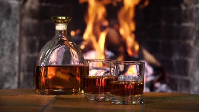壁炉火背景下的威士忌或白兰地酒瓶和玻璃杯